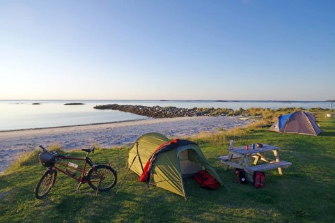 Camping on a quiet beach at dusk with tent, bike and picnic table, cycling holidays, adventure