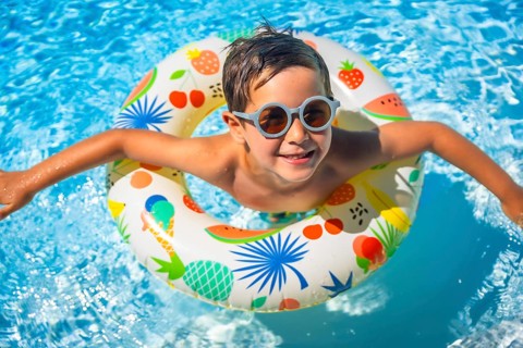 Top view of a happy young boy inside a blue swimming pool with swim goggles and a float