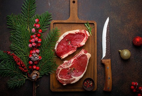 Two raw uncooked meat beef steaks on wooden cutting board with knife and seasonings on dark rustic