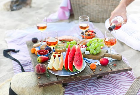 Crop male serving pink wine having picnic with delicious snacks and fruit on sandy beach