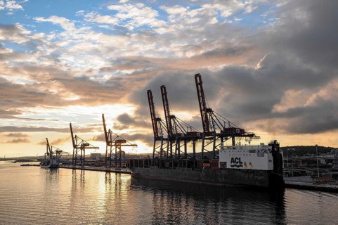 Harbour at sunset with cranes and a large ship, clouds in the sky are reflected in the water,