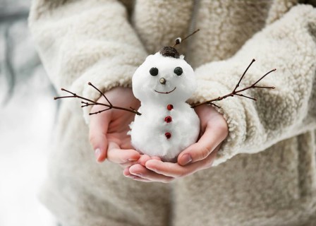 Little snowman, decorated with twigs and berries, held in children's hands in a winter garden with