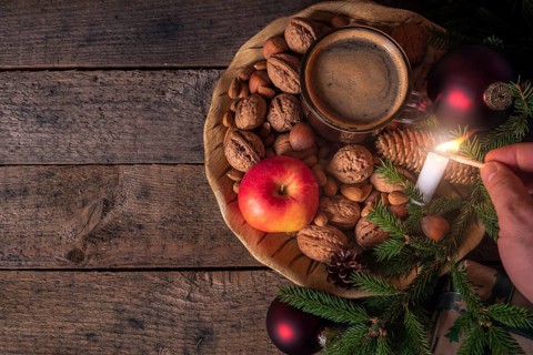 Christmas table with a wooden plate full with nuts, apples, a cup of coffee and green fir twigs,