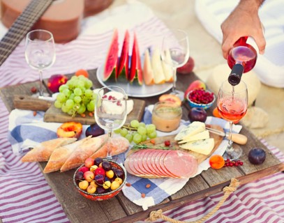Crop male serving pink wine having picnic with delicious snacks and fruit on sandy beach