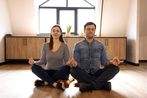 Peaceful adult couple in sportswear sitting on the floor in lotus pose with eyes closed, meditating
