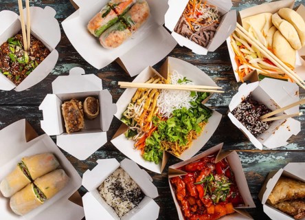 Assorted Chinese dishes in paper delivery boxes: sweet and sour chicken, dim sum, spring rolls,