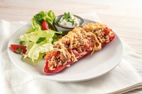 Red bell pepper baked with rice, tuna, tomatoes and cheese, lettuce salad and dip on a white plate