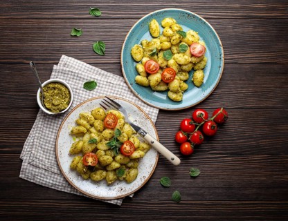Gnocchi in plates with green pesto sauce, tomatoes and herbs on rustic wooden background, close up,