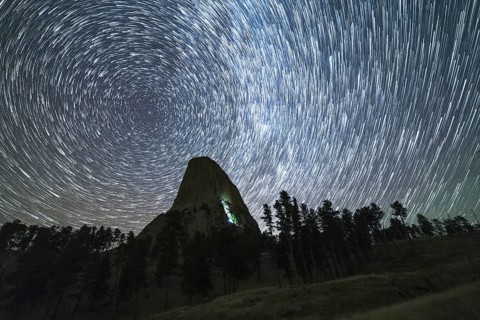 Star Trails over Devils Tower Butte at Night. Light Flare of Climbers on a Wall. Wyoming, USA,