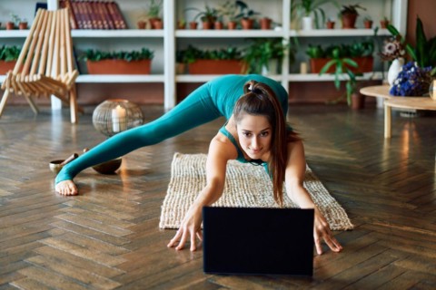 Young sporty woman practicing yoga at home watching online exercises on her laptop. Healthy