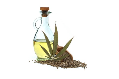 Hemp (Cannabis sativa) leaf in front of cannabis oil in glass decanter and hemp seeds isolated on