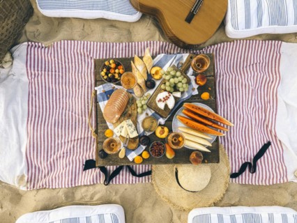 Various tasty food and drinks placed on wooden table during summer picnic on sandy beach at sunset