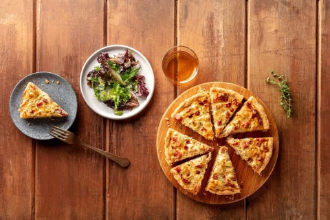 An overhead photo of a quiche with wine and mesclun salad leaves on a dark rustic wooden background