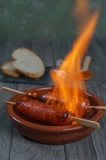 Typical spanish tapa, chorizo on fire in an earthenware casserole with slices of bread in the