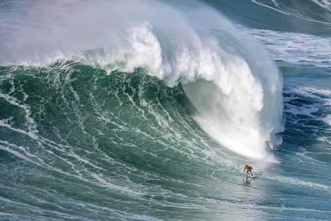 A surfer rides a crashing wave, Nazaré, Portugal, Europe