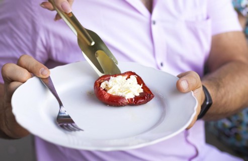 Baked red-colored bell peppers stuffed with herbs and cheese on a dish on summer outdoors party.