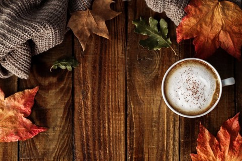 Hot coffee cappuccino, blanket and autumn leaves on old wooden background. Vintage toning. Seasonal