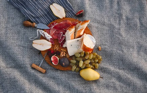 Top view of wooden board with pieces of bread pear figs nuts green grape and delicious cheese on