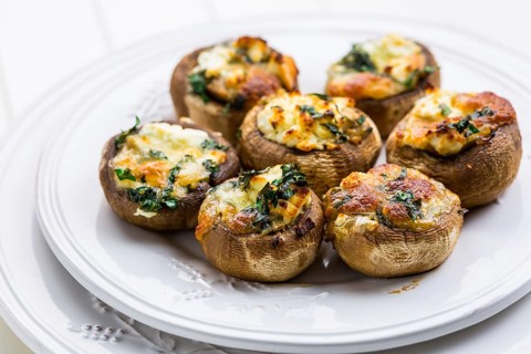 Baked champignons mushrooms, filled with cheese, parsley and roasted garlic on white plate.