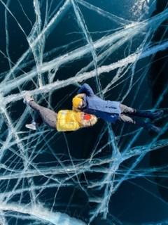 Happy couple lying on the frozen winter Lake Baikal wearing winter clothes. Transparent ice. Travel