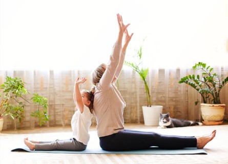 Mature woman and little girl sitting on mat in lotus pose and meditating while doing yoga in