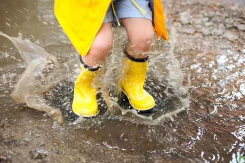 Little girl wearing yellow boots and coat jumping in rainy day