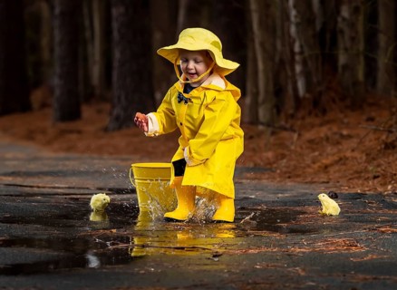 A small child plays in the rain while little chicks try to get a drink of water