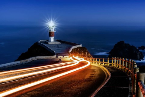 Bright trailing car lights lead to Cabo Ortegal lighthouse at night