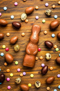 Chocolate Easter bunny with sweet chocolate eggs and colorful sweets on wooden background