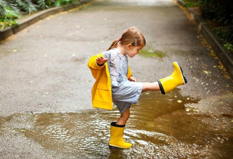Little girl wearing yellow boots and coat jumping in rainy day