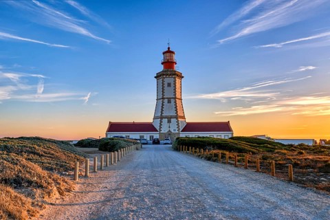 Beautiful of coastal lighthouse in warm colors of sunset, a clear path leading to it. Clear blue