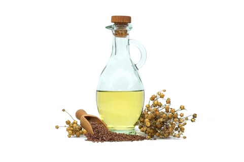 Linseed oil in glass decanter and linseed in wooden scoop near bunch of flax plants isolated on