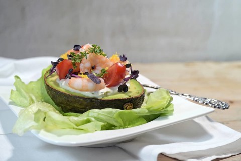 Filled avocado with shrimps, tomatoes, mayonnaise and cress garnish on lettuce and a white plate,