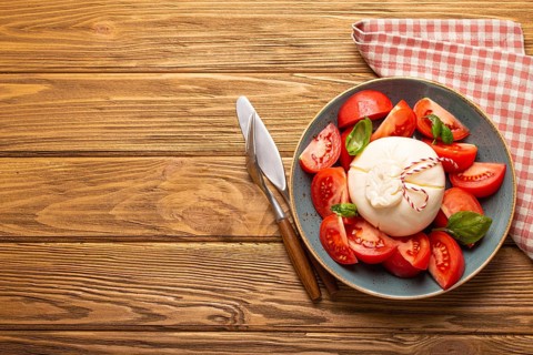 Italian salad with fresh tomatoes, burrata cheese, basil and olive oil served on ceramic plate on