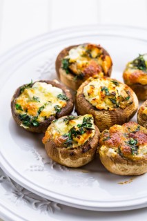 Baked champignons mushrooms, filled with cheese, parsley and roasted garlic on white plate.