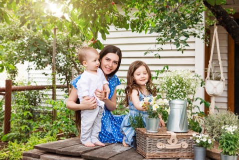 Young delighted mother sitting in armchair with adorable little siblings on terrace of country