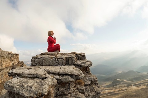 A beautiful girl meditates in a lotus pose sitting on a rock above the clouds against the backdrop