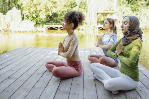 Group of teenages is engaged in fitness on pier by the lake or river. Young and positive girls go