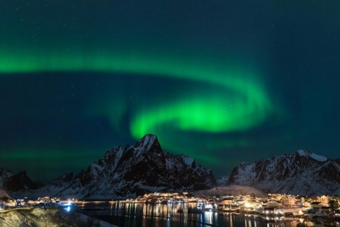 Dancing green polar lights over the village Reine on the Lofoten islands in Norway at night in