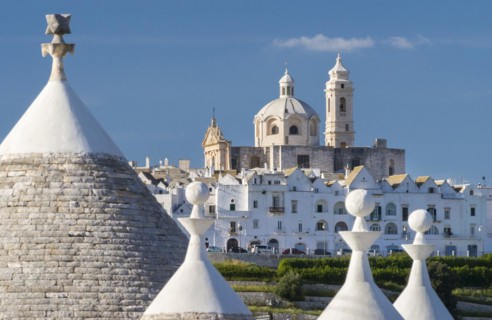 View through trulli, round conical houses, to Locorotondo with the neoclassical church San Giorgio
