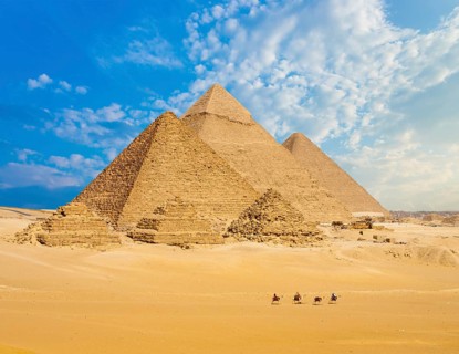 All Egyptian Pyramids from distance with row of camels walking in foreground in Giza, Cairo, Egypt.