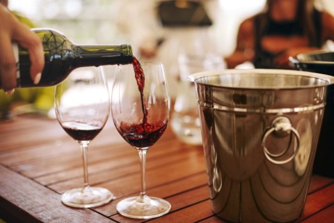 Glasses with different types of wine and human hands holding wine glasses in the background.