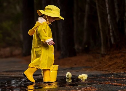 A small child plays in the rain while little chicks try to get a drink of water