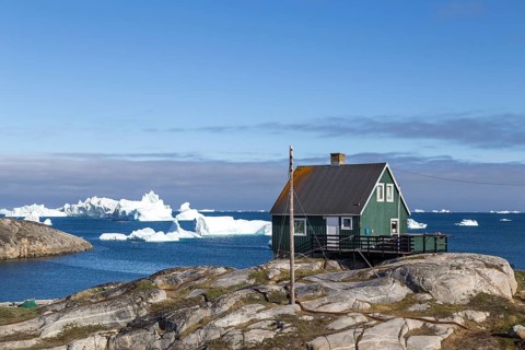 Qeqertarsuaq, Greenland, July 05, 2018: A green wooden house with icebergs in the background, North