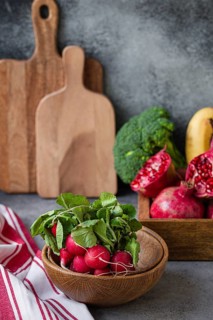 Bunch of fresh raw radish in wooden bowl on kitchen table with fresh fruit, greens, vegetables in