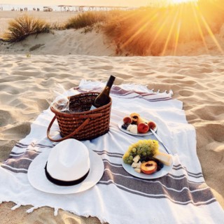 Romantic picnic on sandy beach at amazing evening sunset, blanket with wine bottle and glasses in