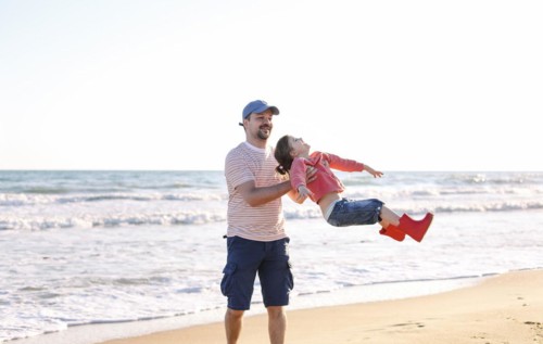 Loving father playing with his adorable little daughter on beach, swinging her around, dad and