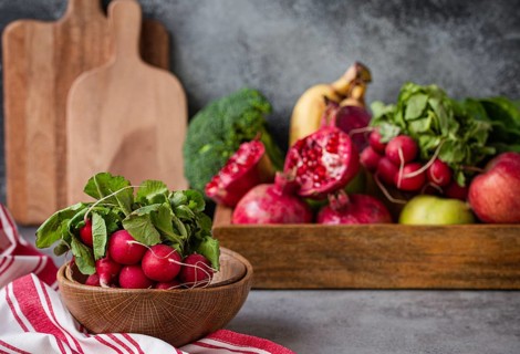 Bunch of fresh raw radish in wooden bowl on kitchen table with fresh fruit, greens, vegetables in