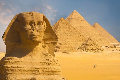 A closeup of the face of the Great Sphinx with a set of pyramids in the background on a beautiful