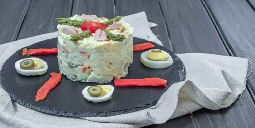 Black slate plate with ensaladilla rusa or Russian salad typical spanish tapa garnished with red